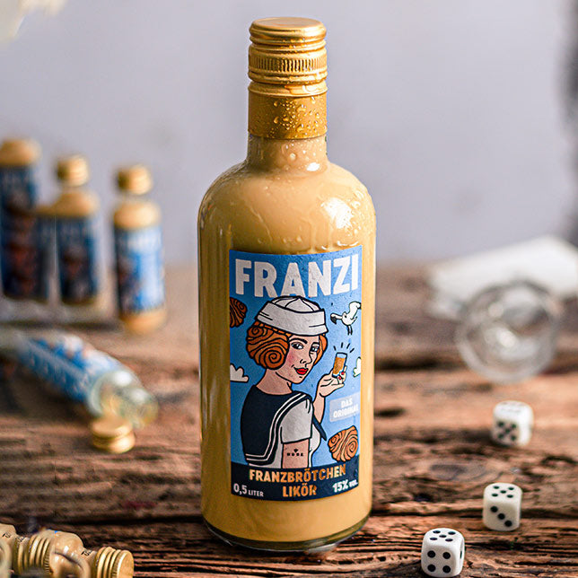 Eine 0,5l Flasche Franzi Franzbrötchenlikör auf einem Holztisch mit Würfeln und leeren und gefüllten Franzi Mini Flaschen im Hintergrund