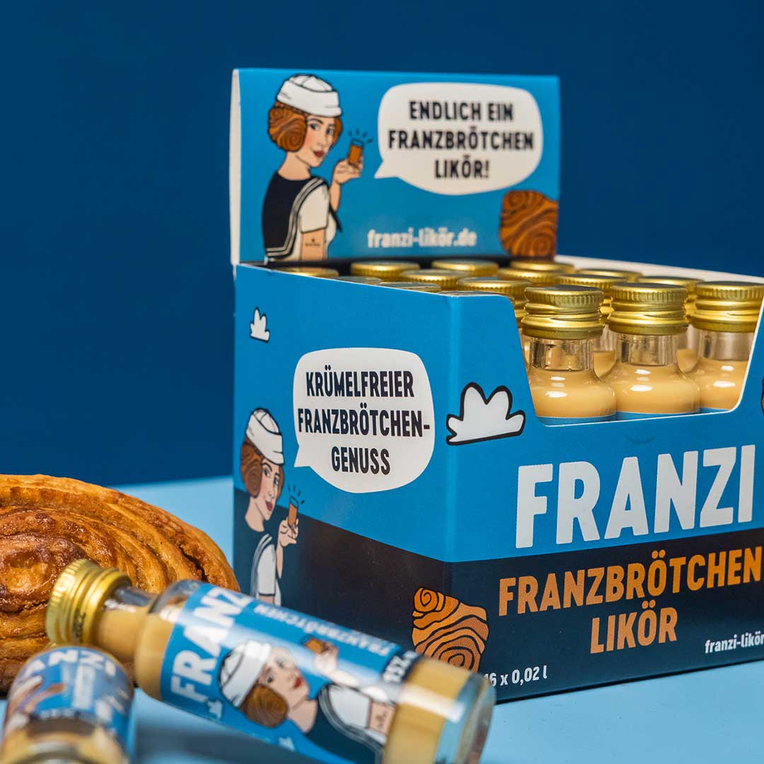 Eine gefüllte Franzbrötchenlikör Mini-Box mit einem Franzbrötchen daneben und zwei kleinen Flaschen Franzi  davor